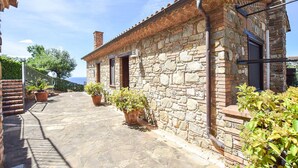 Un bâtiment en pierre avec un toit en tuiles, une cheminée et un petit porche agrémenté de plantes en pot.
