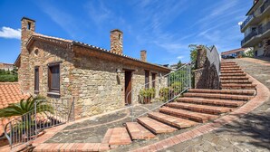 Un bâtiment en pierre avec un toit recouvert de tuiles, un escalier menant à une porte et une rambarde en métal.