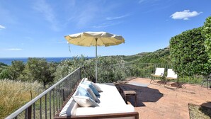 Une terrasse avec un canapé blanc, un parasol et deux chaises, offrant une vue panoramique sur un paysage magnifique et la mer.