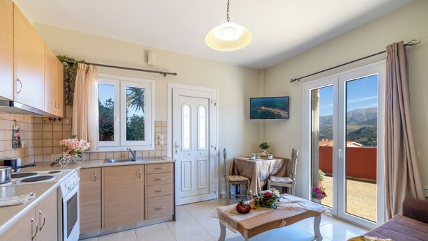 A modern kitchen with a dining area, a sofa, and a table with a view of the outdoors.