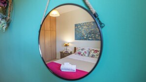 A bedroom with a bed, a nightstand, a lamp, a mirror, and a painting on the wall.
