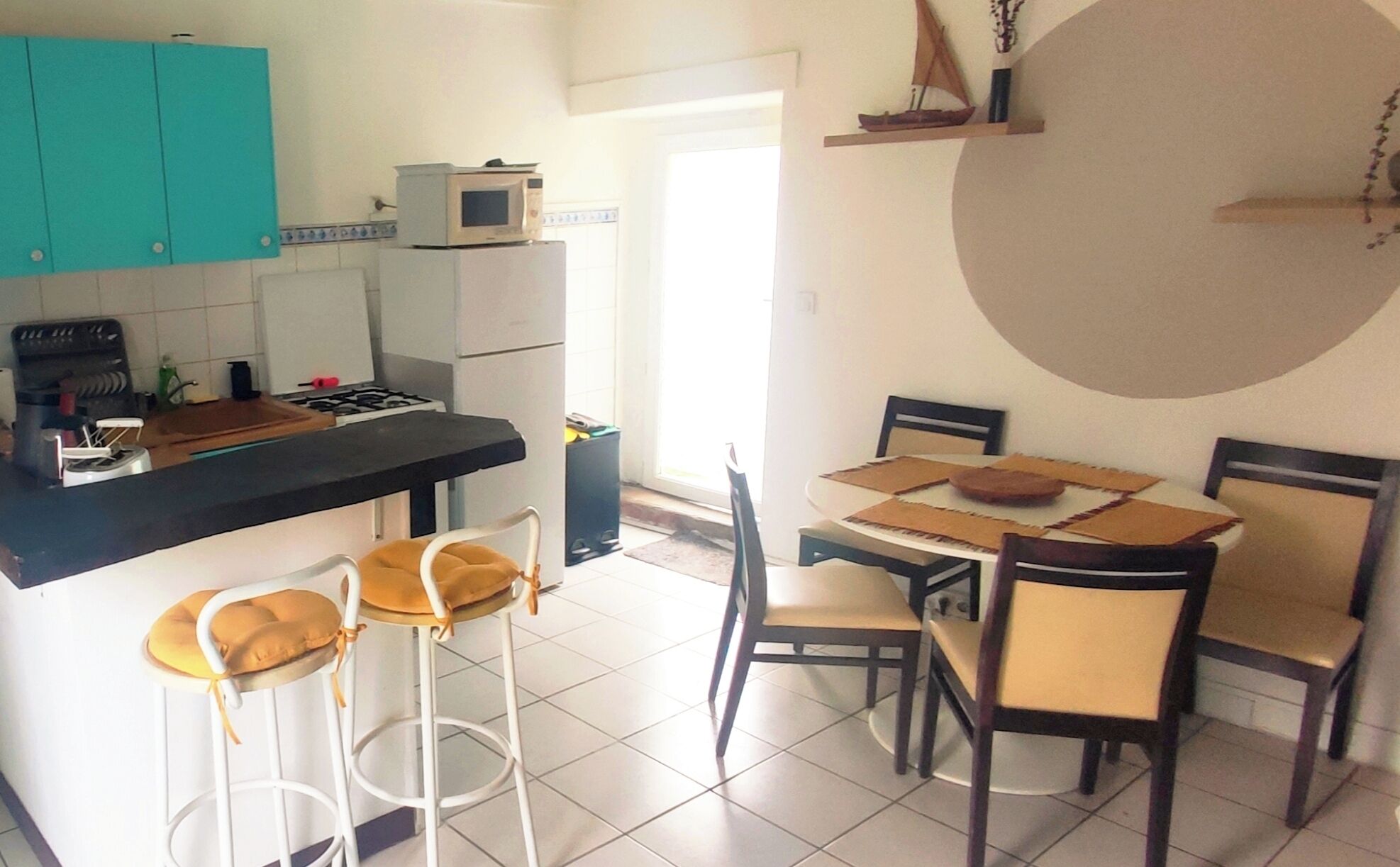 Una cocina con estufa, microondas y gabinetes color verde azulado. Incluye una mesa de comedor con sillas y una pequeña isla con taburetes.