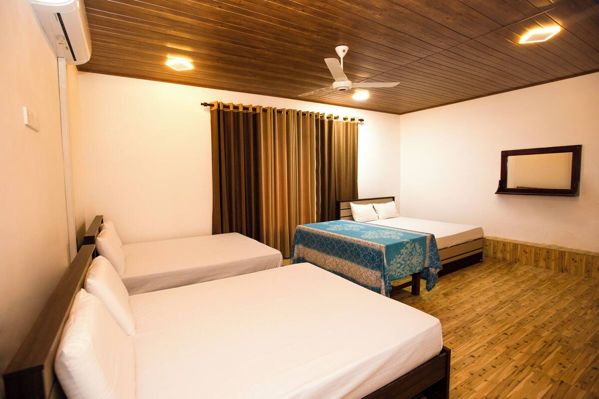 A hotel room with two single beds, a ceiling fan, wooden flooring, and a large window with curtains.