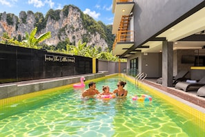 Ein Swimmingpool mit klarem Wasser, umgeben von einer schwarzen Mauer mit einem Schild, und eine gebirgige Landschaft im Hintergrund.