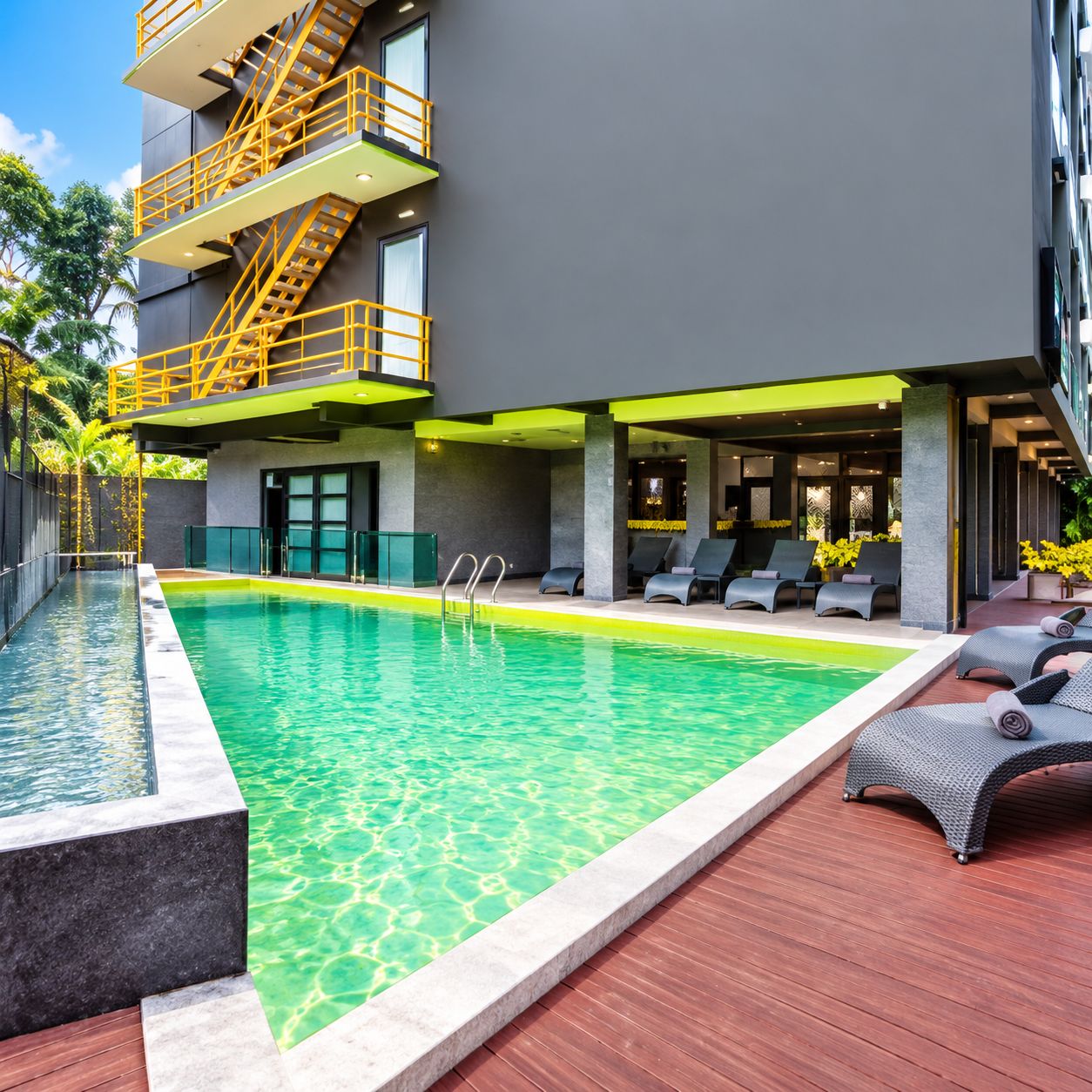 Un hotel moderno con piscina, asientos exteriores y un balcón de varios niveles.