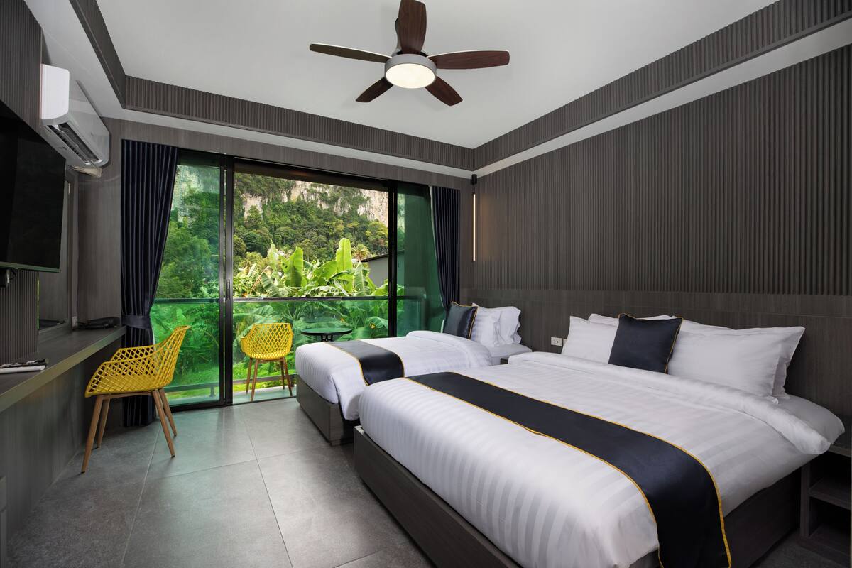 Habitación de hotel moderna con una cama grande, un escritorio con silla y un balcón con vistas a zonas verdes.