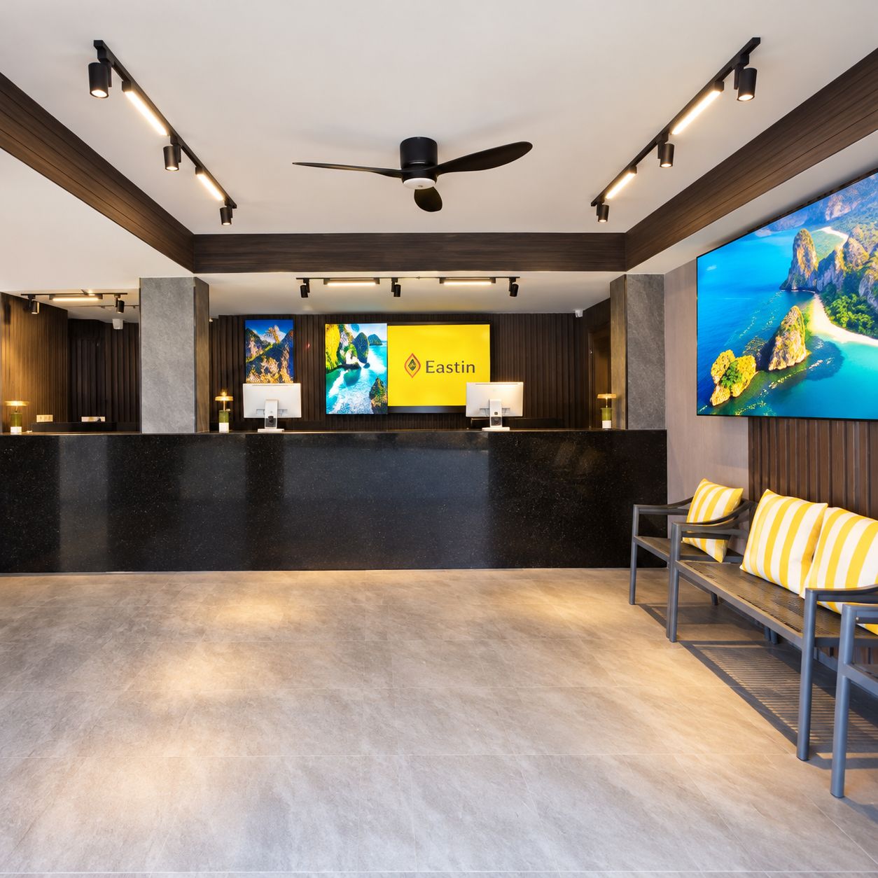 A hotel reception area with a reception desk, a ceiling fan, and a large screen displaying a scenic view.