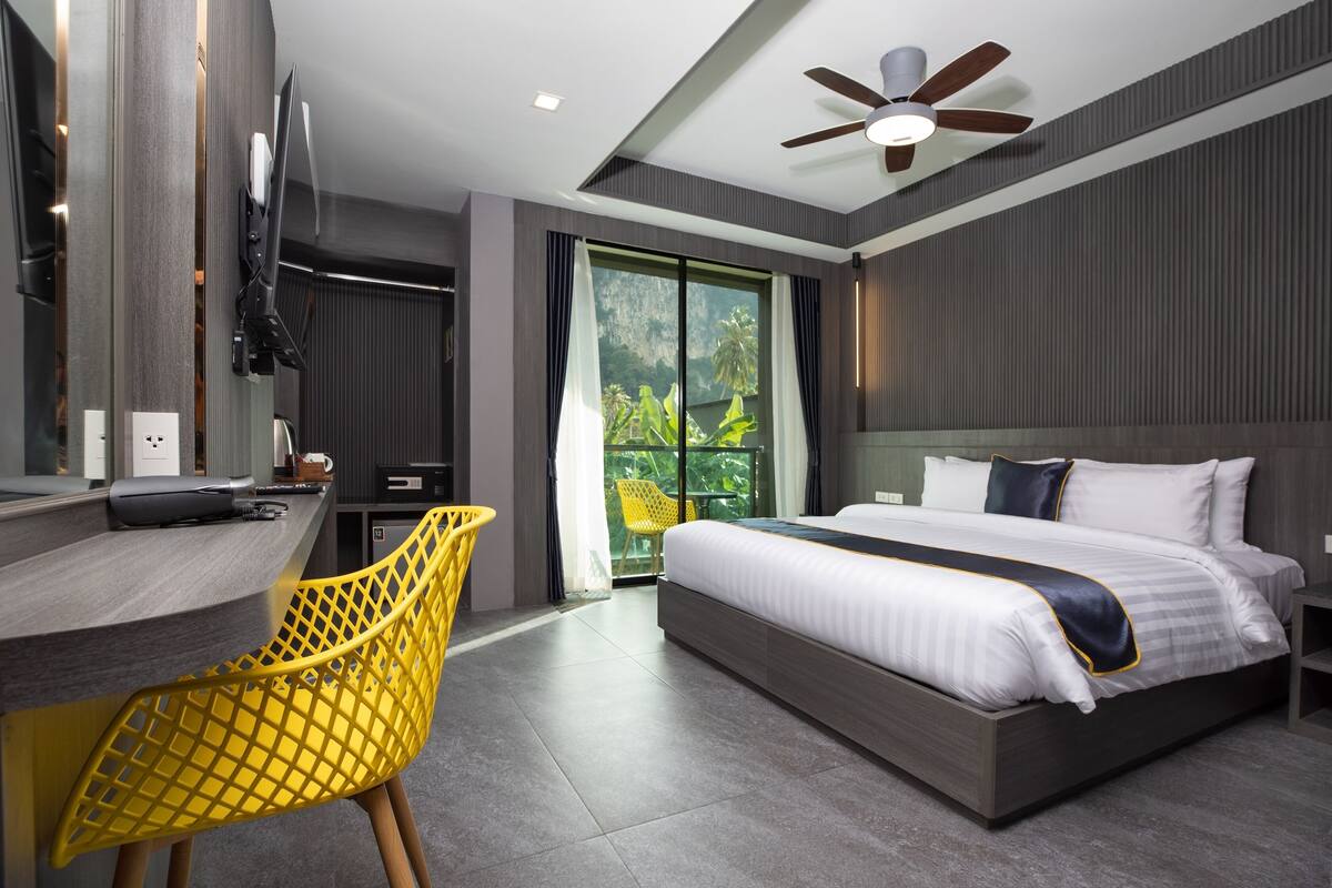 Habitación de hotel moderna con una cama grande, un escritorio con silla, un ventilador de techo y vistas a zonas verdes por la ventana.