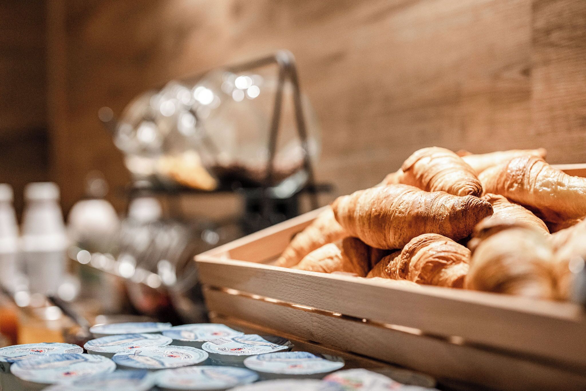 Een houten kist gevuld met croissants en een presentatie van yoghurtbekers.