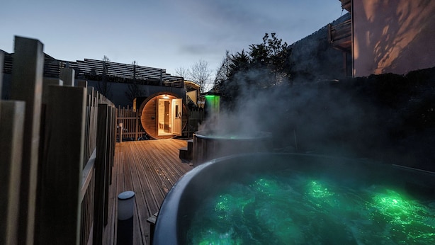 A hot tub with green lighting, surrounded by a wooden deck and a wooden fence. - Hotel Garni Meledrio (Dimaro Folgarida)