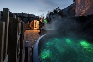 A hot tub with green lighting, surrounded by a wooden deck and a wooden fence. - Hotel Garni Meledrio (Dimaro Folgarida)