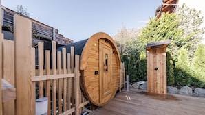 A wooden cabin with a large circular door, a wooden deck, and a small wooden structure in the background. - Hotel Garni Meledrio (Dimaro Folgarida)