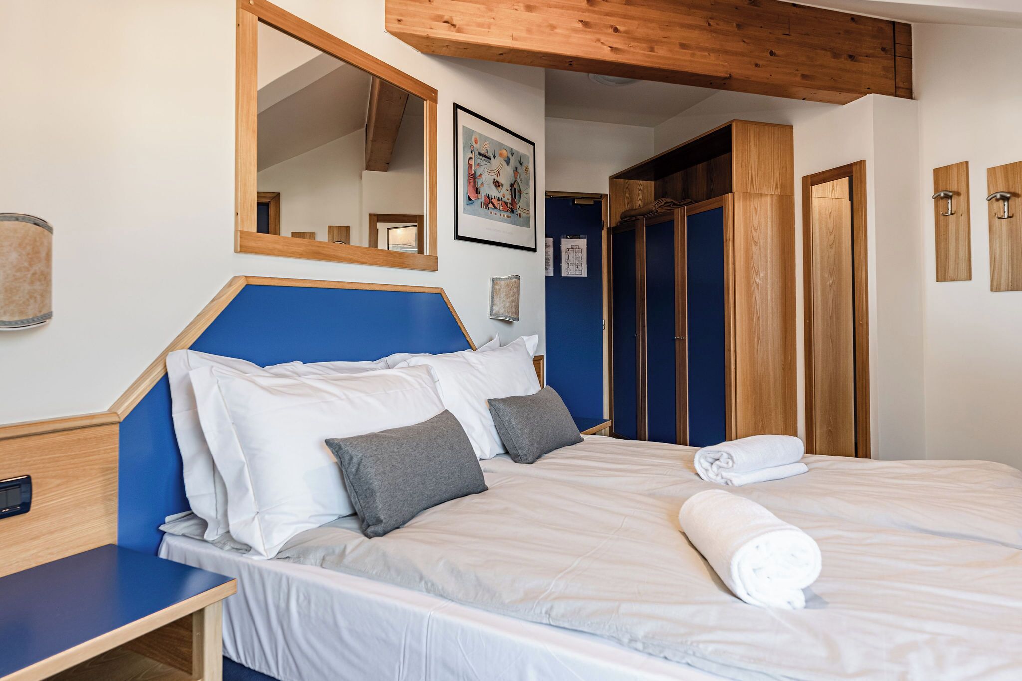 A bedroom with a bed, a wooden headboard, a mirror, and a blue accent wall.