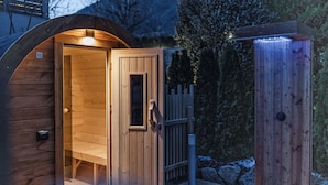 A wooden sauna with a glass door and a bench inside, surrounded by a wooden fence and trees. - Hotel Garni Meledrio (Dimaro Folgarida)
