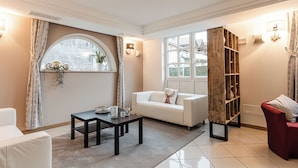 A modern living room with a white sofa, a wooden bookshelf, and a dining table. - Hotel Garni Meledrio (Dimaro Folgarida)