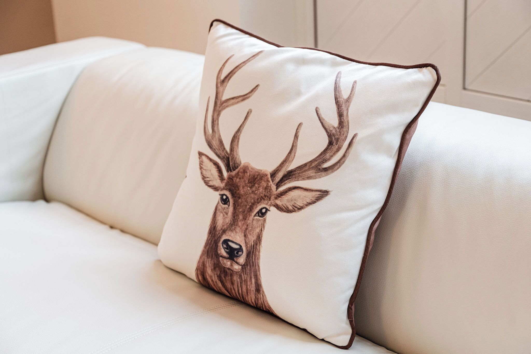 A white sofa with a pillow featuring a deer illustration.