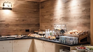 A buffet setup with various food items and beverages, including pastries, fruits, and dairy products, against a wooden wall backdrop. - Hotel Garni Meledrio (Dimaro Folgarida)