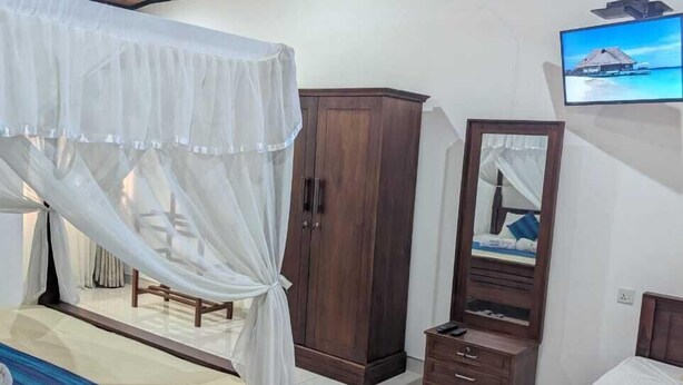 A bedroom with a bed, a wardrobe, a TV, and a ceiling fan. - GG Lodge (Mirissa)