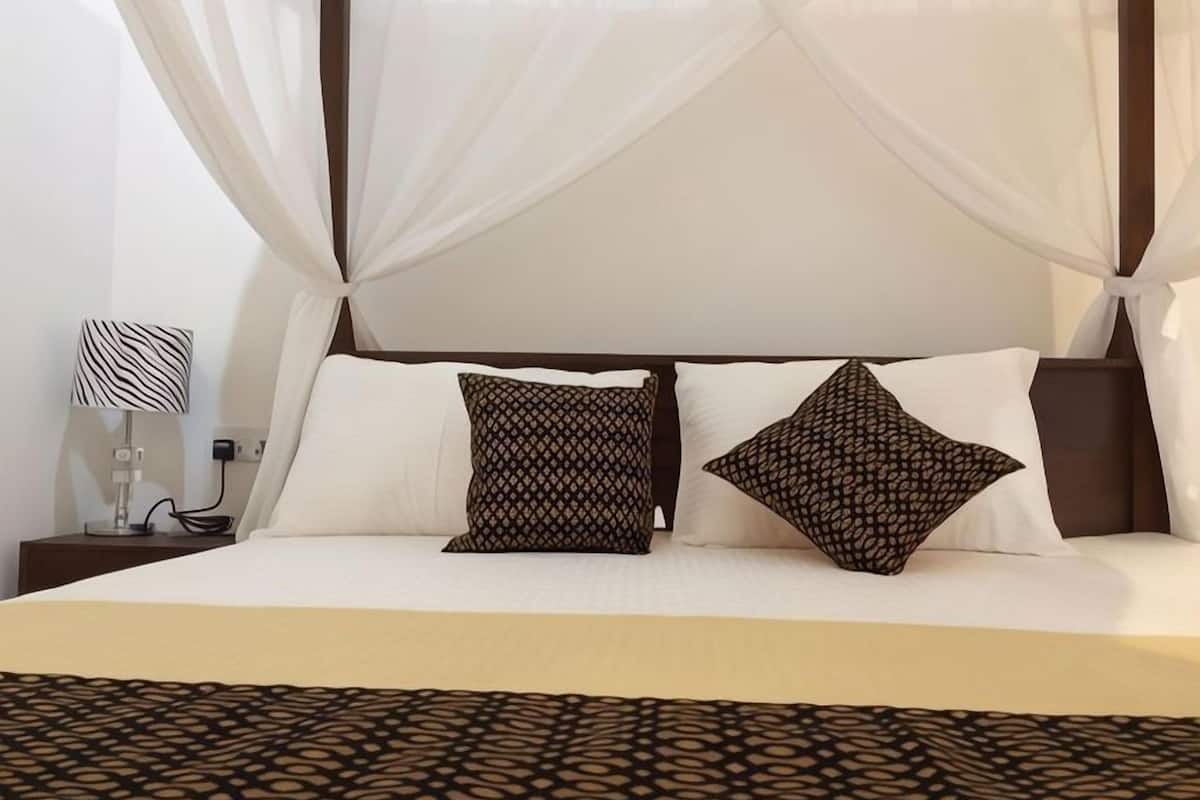 A bed with a canopy, two patterned pillows, a bedside lamp, and a patterned bedspread.
