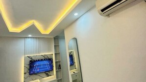 A modern room with a flat-screen TV mounted on a marble-patterned wall, a built-in shelving unit, and a large mirror. - Studio(S3)@LEKKI PHASE 1, 24/7 Pwr by NgoZiLiving

 (Lekki)