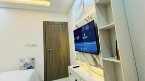 A modern bedroom with a TV mounted on a marble wall, a wooden door, and a white bedside table. - Studio(S3)@LEKKI PHASE 1, 24/7 Pwr by NgoZiLiving

 (Lekki)