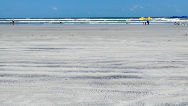 A wide sandy beach with a clear blue sky and ocean waves. - Pousada Temporada no Atalaia (Salinópolis)