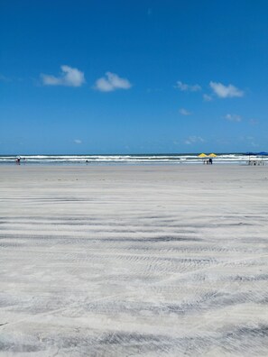 A wide sandy beach with a clear blue sky and ocean waves. - Pousada Temporada no Atalaia (Salinópolis)