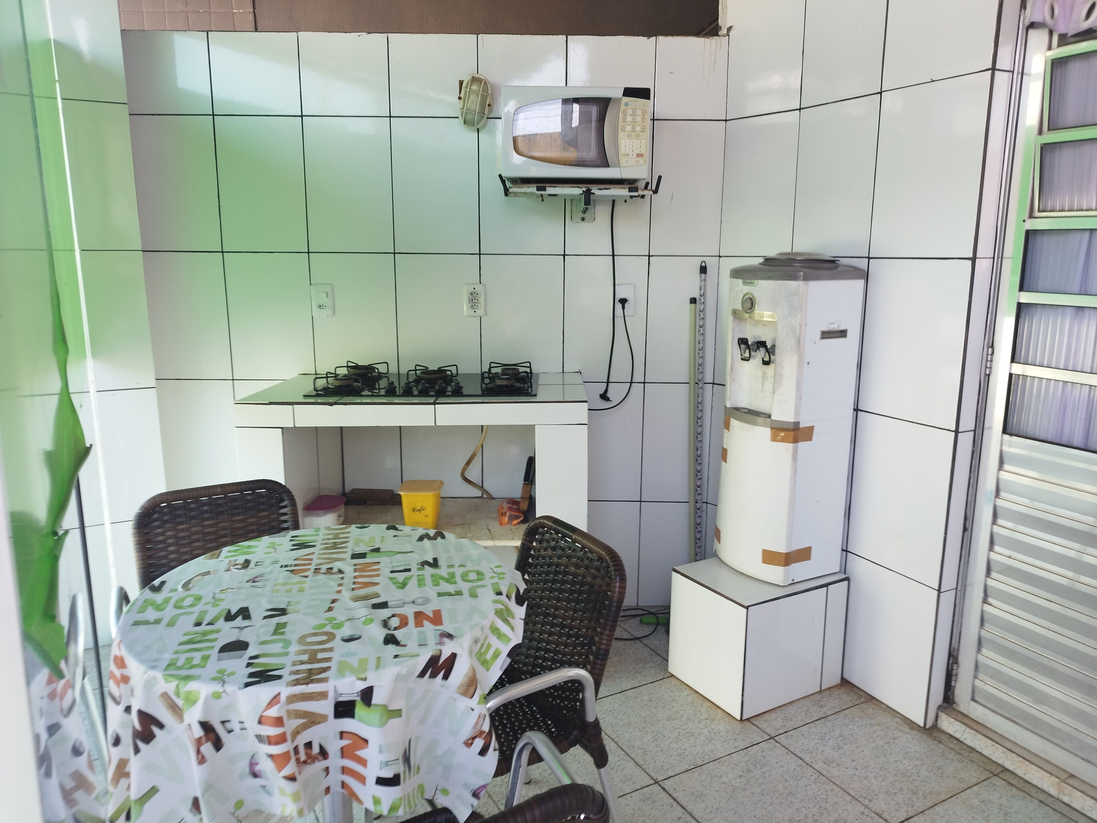 Une cuisine compacte avec un coin repas, comprenant une table recouverte d’une nappe à motifs, un four à micro-ondes, un petit réfrigérateur et une cuisinière à gaz.