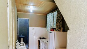 A compact kitchen with a gas stove, a sink, and a refrigerator. There are white plastic chairs and a tiled floor. - Pousada Temporada no Atalaia (Salinópolis)