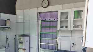 A compact kitchen with a microwave, a sink, and a window with purple curtains. - Pousada Temporada no Atalaia (Salinópolis)