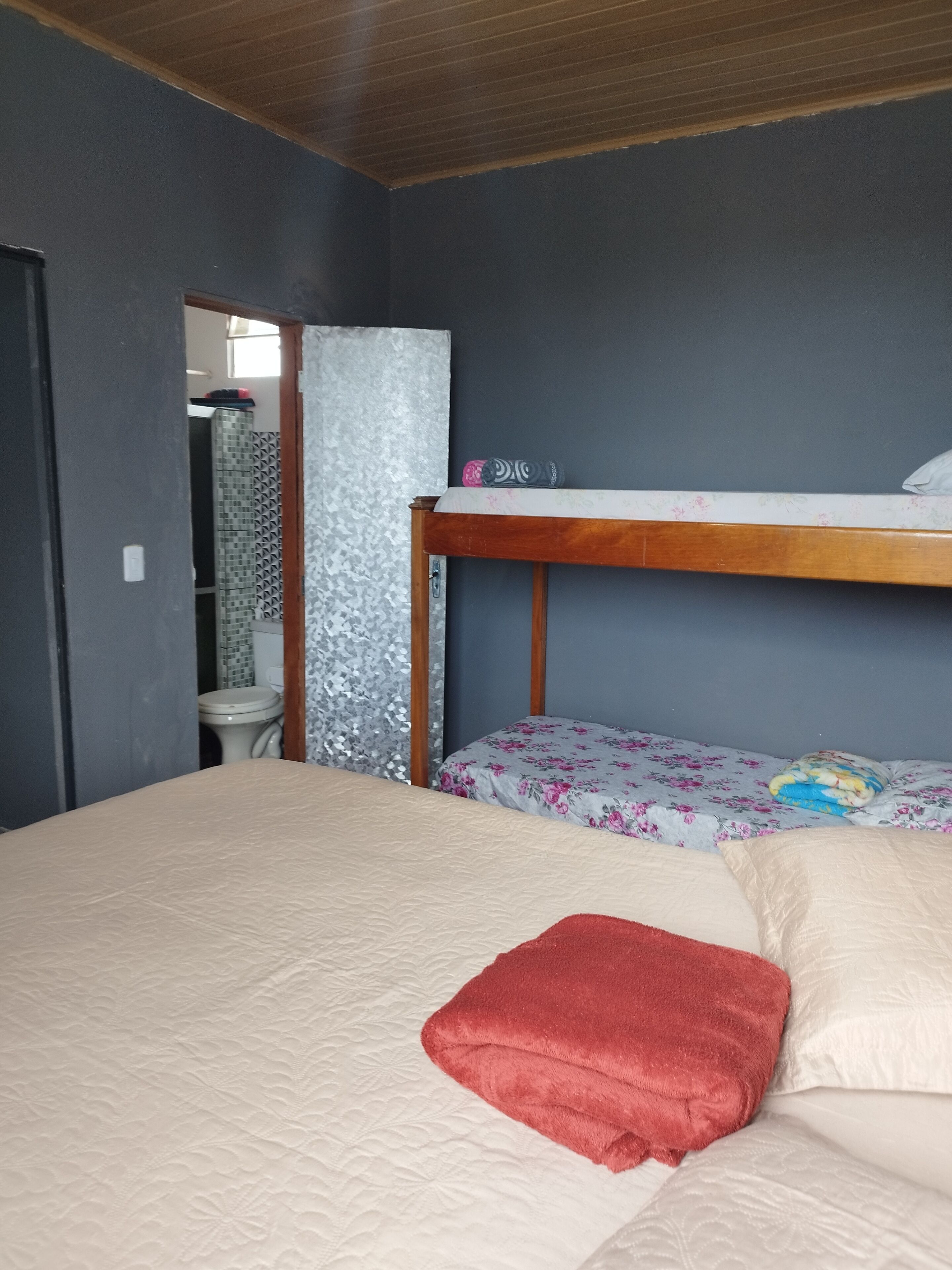 A bedroom with a bunk bed, a wooden headboard, a red towel on the bed, and a bathroom visible through an open door.
