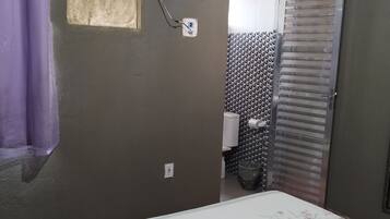 A bedroom with a bed, an air conditioner, a bathroom with a toilet, and a shower area.