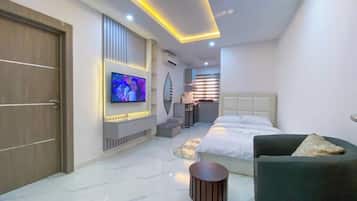 Une chambre d’hôtel moderne avec un grand lit, un téléviseur fixé au mur, un petit coin salon et une salle de bain visible au fond.