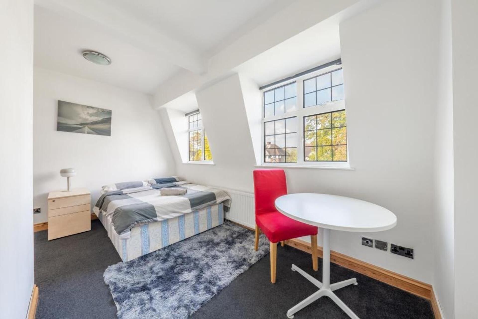 A bedroom with a bed, a desk, a chair, and two windows.