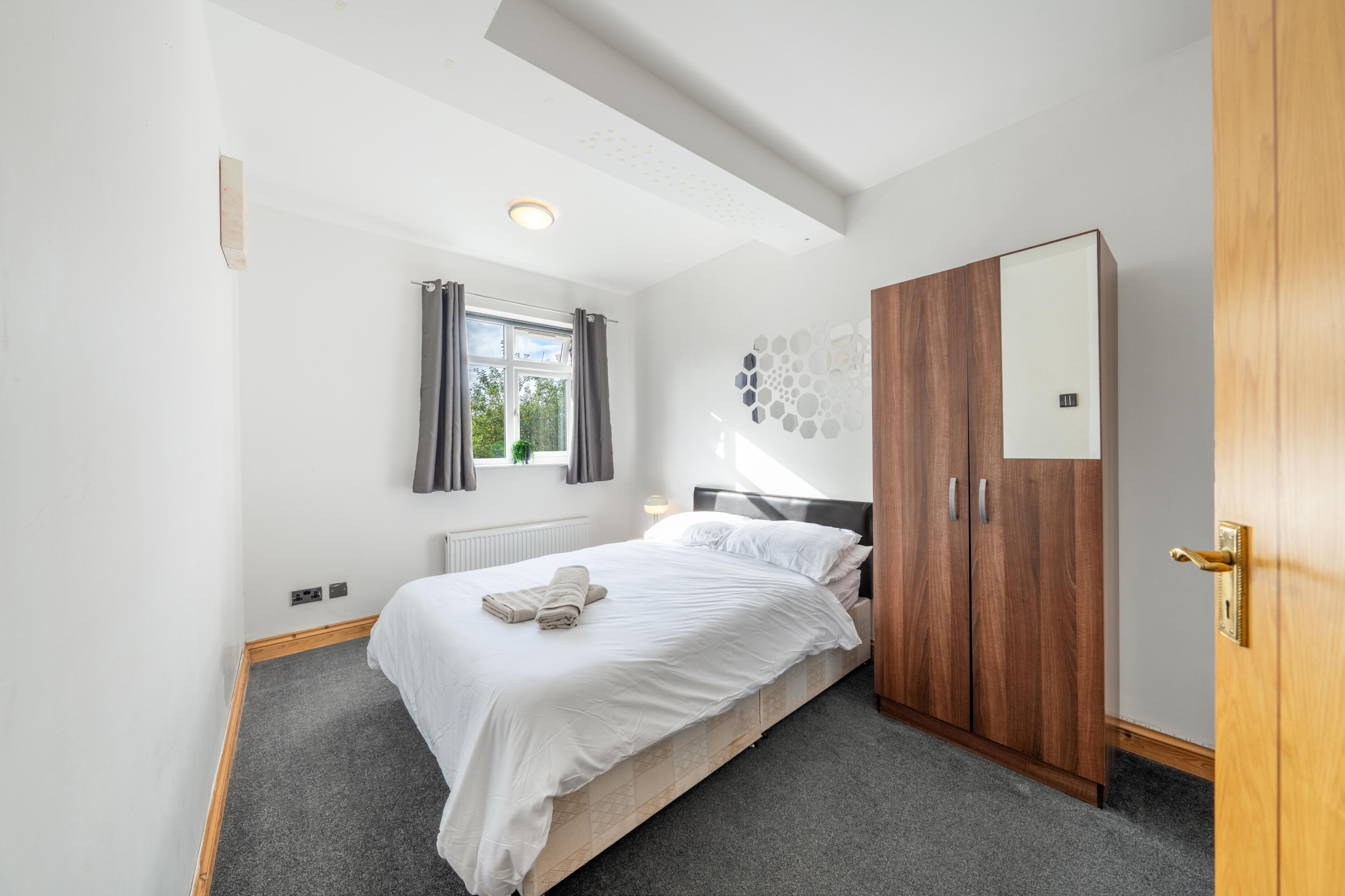 Une chambre à coucher comprenant un lit, une armoire, une fenêtre avec des rideaux et un luminaire fixé au mur.
