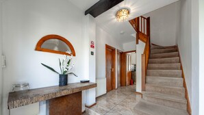 Un couloir avec un escalier en bois, un comptoir d’accueil orné d’une plante en pot et un miroir fixé au mur.