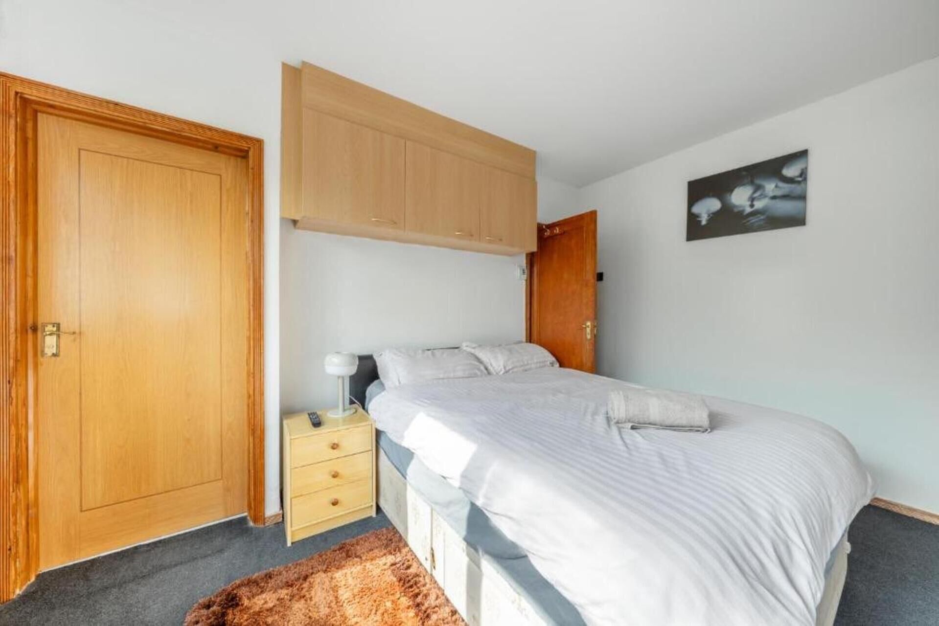 Un dormitorio con cama, mesita de noche, armario y una puerta.