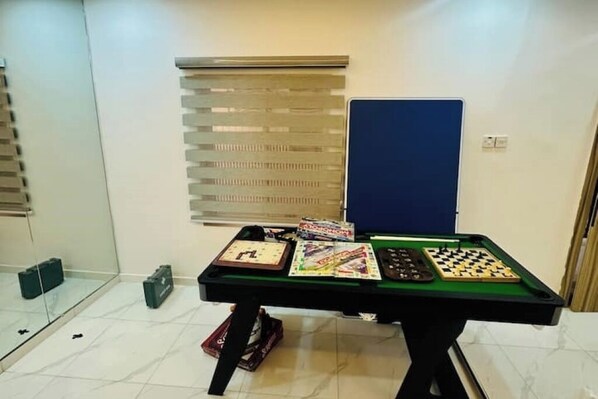 A room with a green pool table, a blue door, and blinds on the windows.