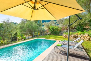 Una piscina con cubierta de madera, sillas de descanso y un paraguas amarillo grande.