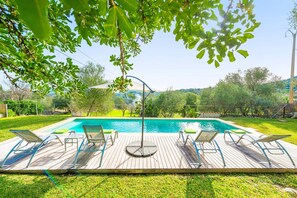 Terraza de madera con piscina, rodeada de follaje y cielo despejado.