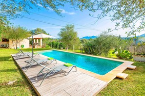 Una piscina rectangular con plataforma de madera y tumbonas de metal.