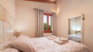 Ein Schlafzimmer mit Bett, einem Fenster mit Vorhängen, einer Nachttischlampe und einem Spiegel.