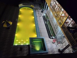 Piscina no terraço, com borda iluminada em amarelo, cercada por um muro de pedra e um edifício com grandes janelas.