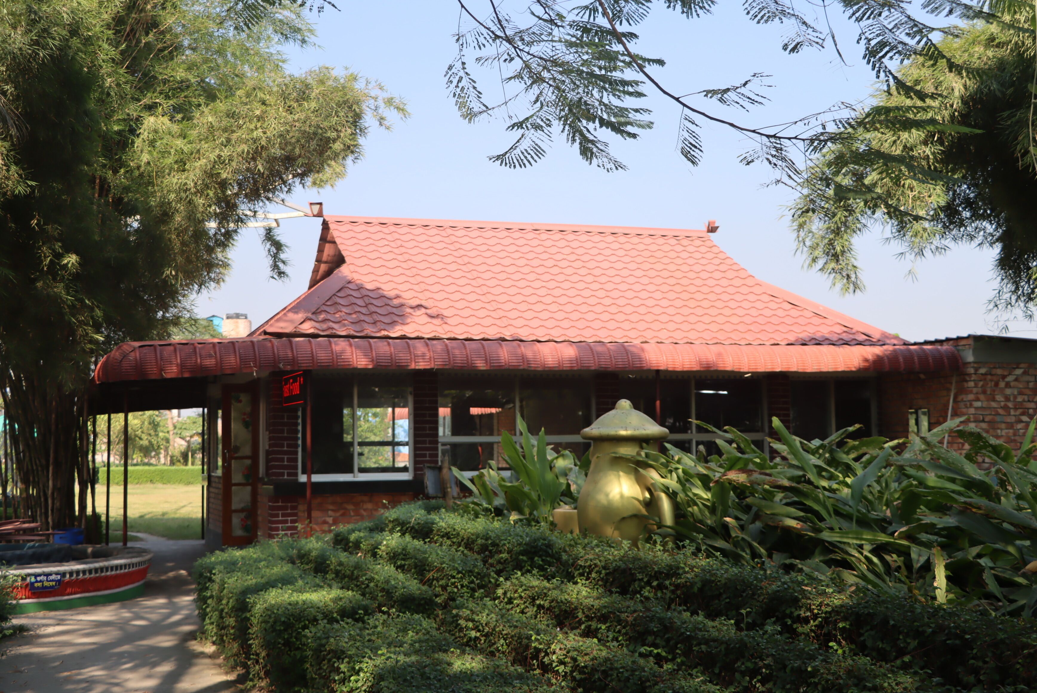 A small brick building with a red tiled roof, surrounded by lush greenery and a fire hydrant.