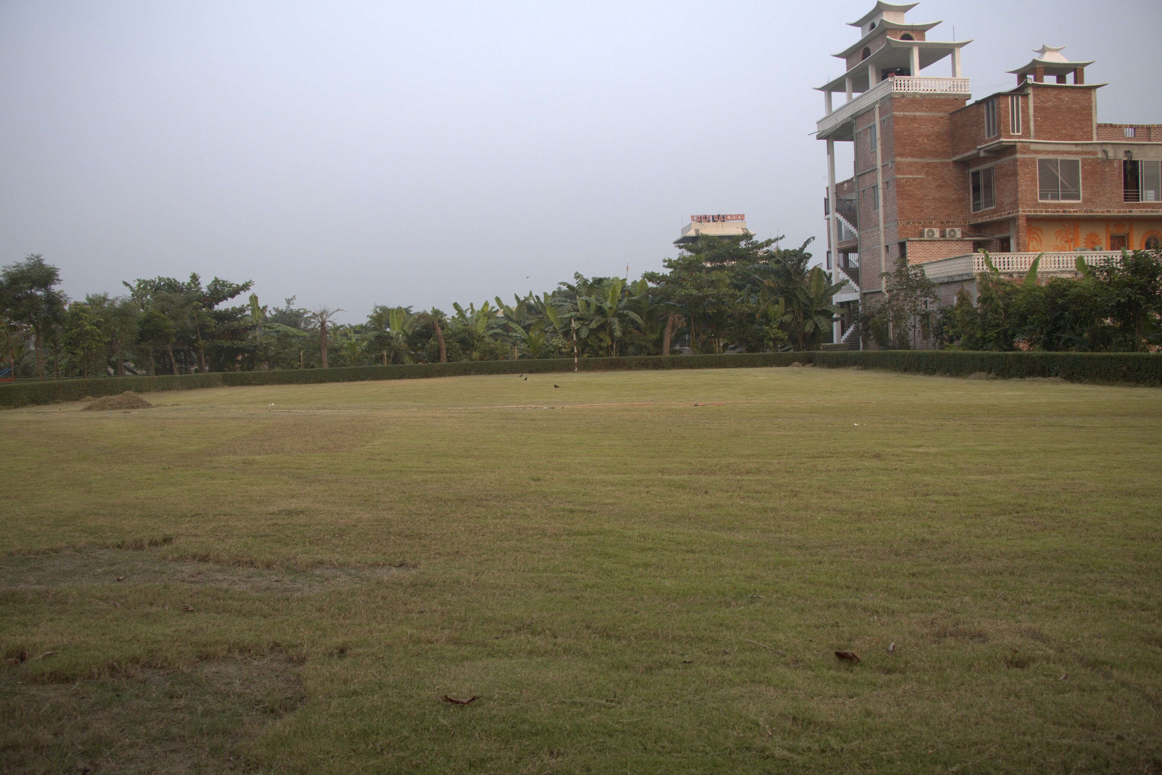 Um extenso campo gramado com um edifício de vários andares ao fundo.