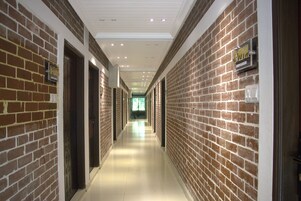 Um corredor comprido e estreito, com paredes de tijolo e painéis de teto brancos, que conduz a um quarto iluminado no final.