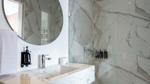 Ein modernes Badezimmer mit Waschtisch aus Marmor, einem großen Spiegel und einer Duschkabine aus Glas.