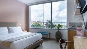 Ein modernes Hotelzimmer mit großem Fenster, einem Bett, einem Schreibtisch und Blick auf die Stadt.