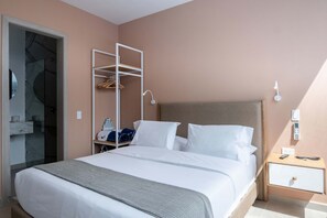 Una habitación de hotel con cama, armario, mesita de noche con lámpara y panel de control en la pared.
