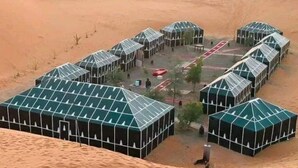 Area desertica con diverse strutture a copertura verde, probabilmente tende o edifici temporanei, disposti a semicerchio.